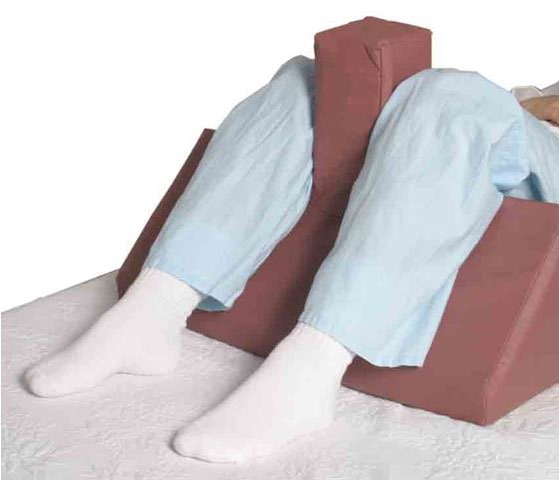A wedge-shaped leg positioner supporting a patient&rsquo;s legs on a bed